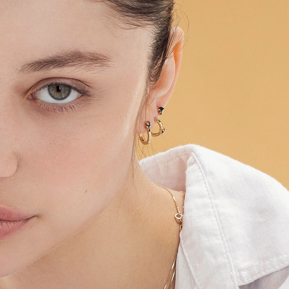 Small gold hoop earrings set with a black diamond close to the ear