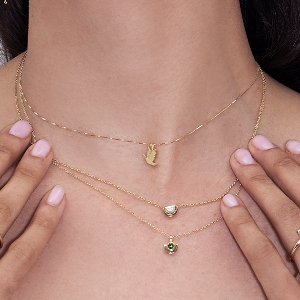 A gold necklace with a dove of peace pendant and an olive leaf