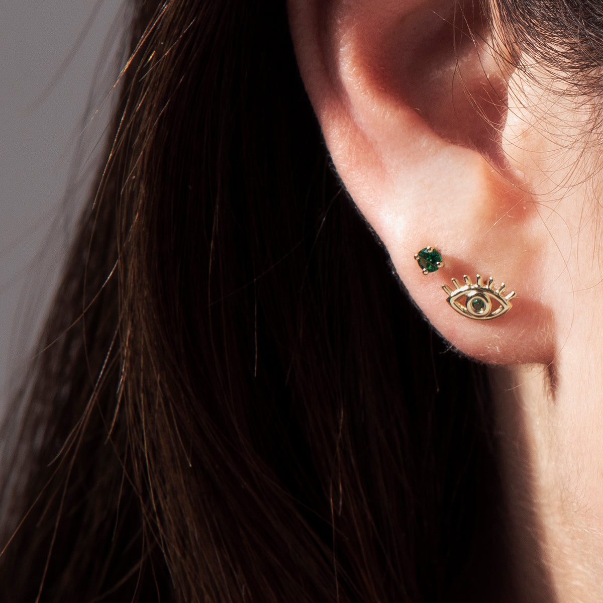 Gold studded earrings in a design against the evil eye, studded with emerald stones