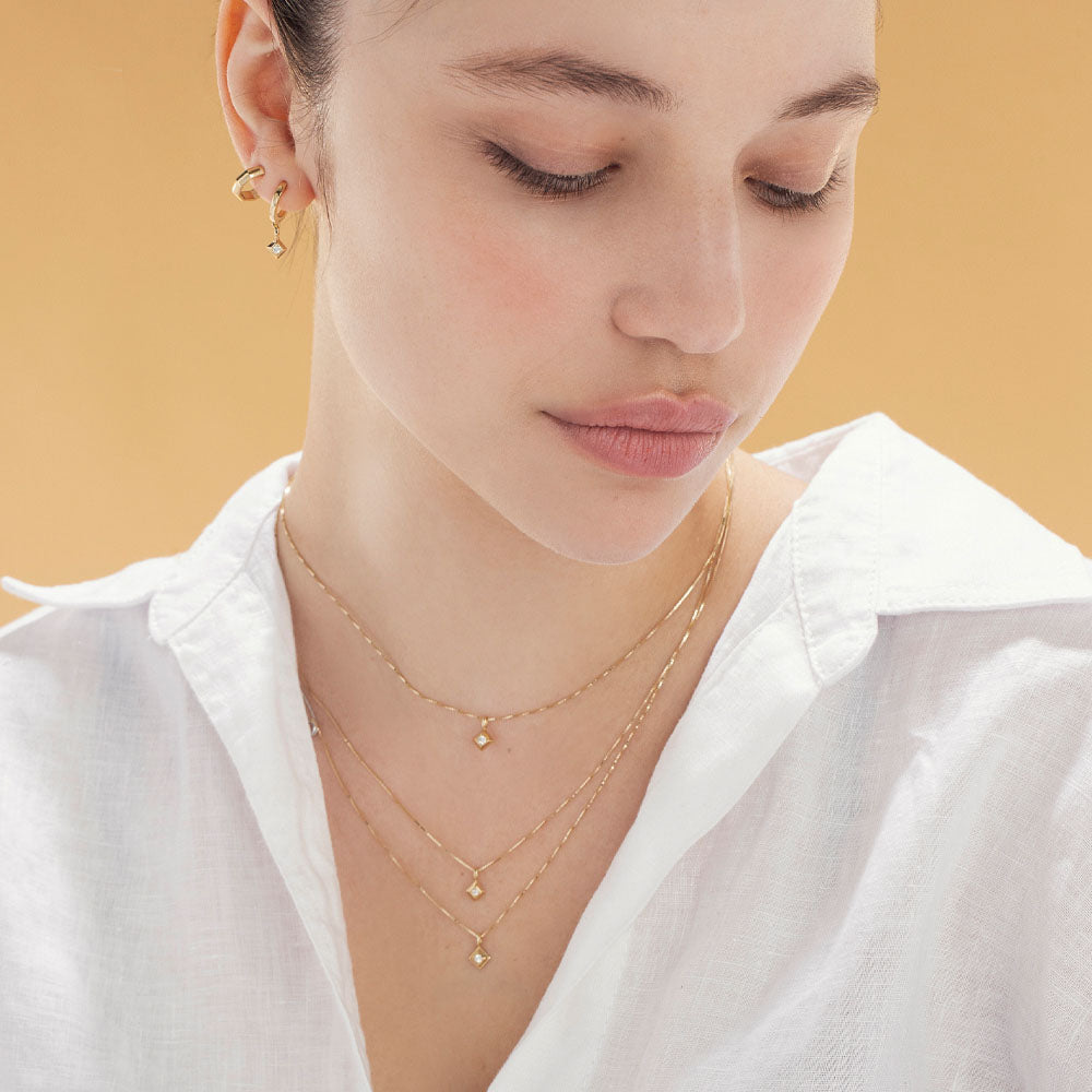 A delicate gold chain with a large square pendant and a 4-point diamond in the center