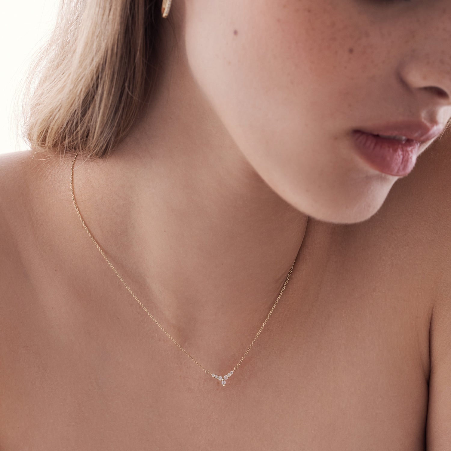 A gold necklace with a V-shaped pendant studded with diamonds reminiscent of a flower