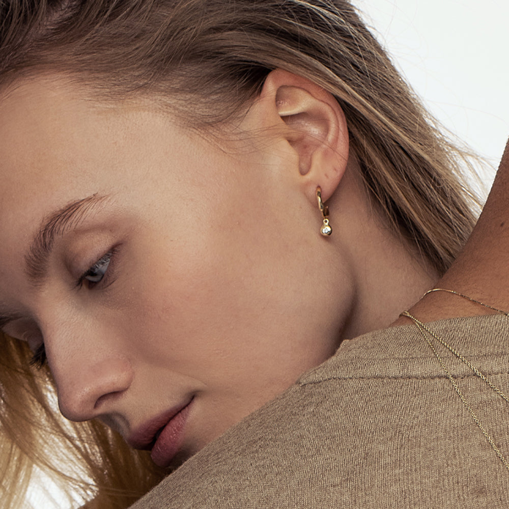 Small gold amorphous hoop earrings with a 4-point diamond pendant in an asymmetrical gold frame