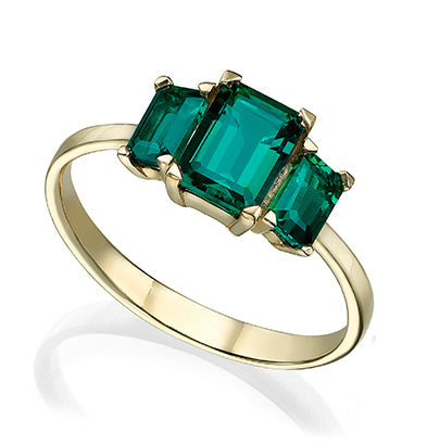 A gold ring set with three rectangular Chatham emeralds