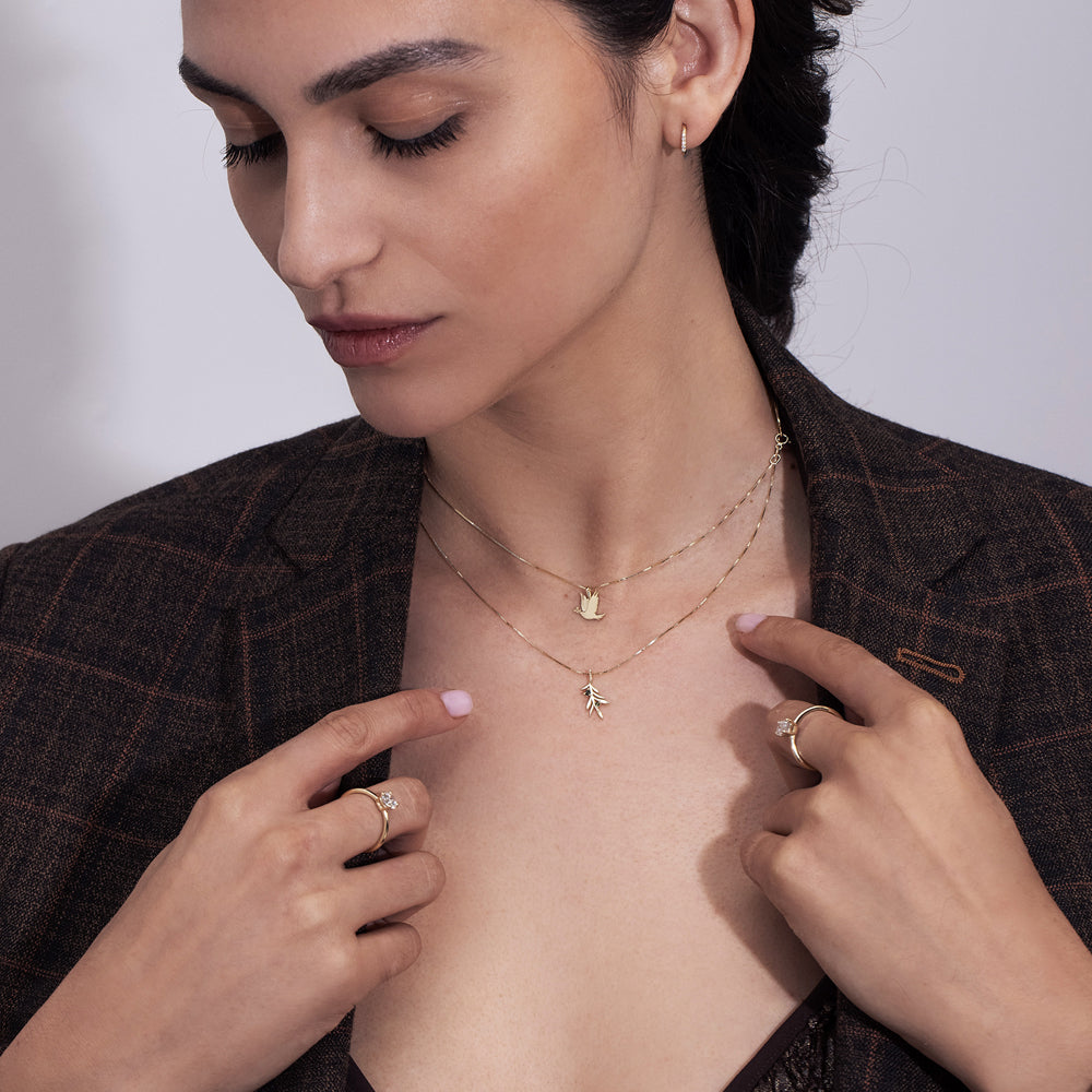 A gold necklace with a dove of peace pendant and an olive leaf