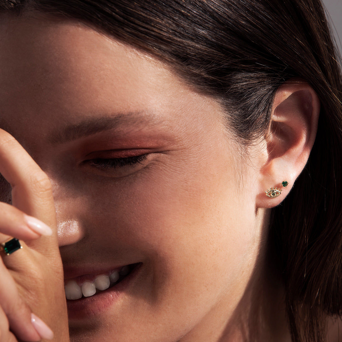 Gold studded earrings in a design against the evil eye, studded with emerald stones