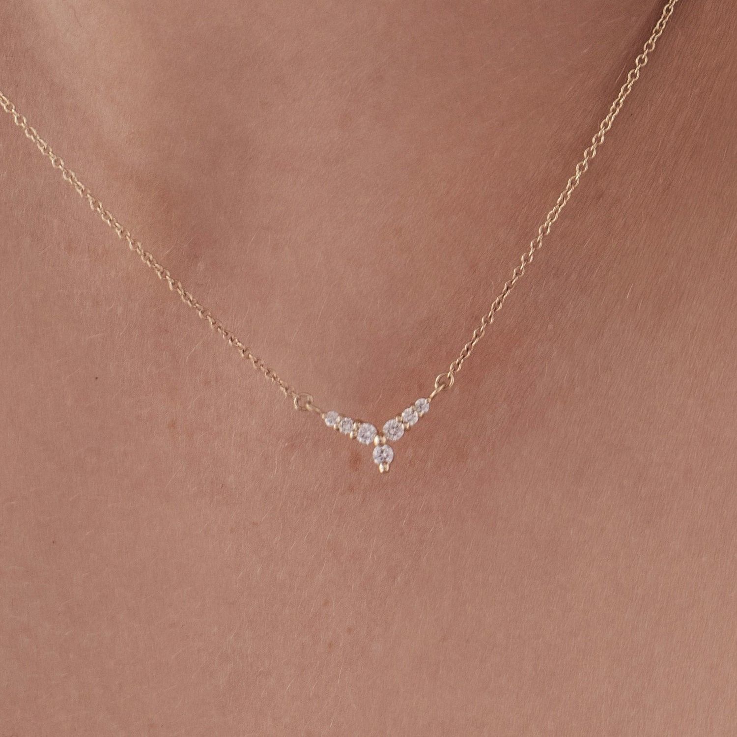 A gold necklace with a V-shaped pendant studded with diamonds reminiscent of a flower
